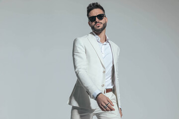 unshaved cool man wearing white stylish suit holding arms in fashion pose