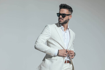 sexy young man in white suit with open collar shirt buttoning jacket