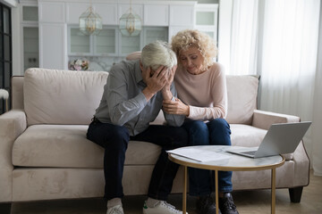 Frustrated desperate mature couple getting bad news, bank, eviction notice, medical test result, touching head, covering face, giving support, empathy, comfort. Sharing problems
