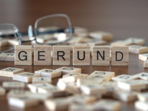 gerund word or concept represented by wooden letter tiles on a wooden table with glasses and a book