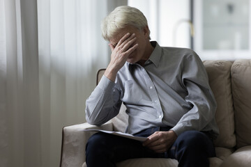 Desperate depressed senior elder man getting bad shocking news from paper documents, sitting on...