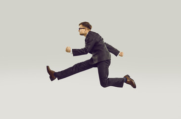 Crazy young businessman in chasing his career running fast isolated on gray background. Profile...