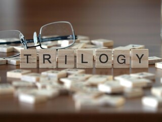 trilogy word or concept represented by wooden letter tiles on a wooden table with glasses and a book