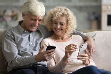 Joyful happy mature married couple using two mobile phones, learning to use online app together,...
