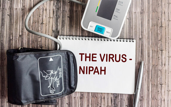 The word about the Nipah virus on a notepad, next to a blood pressure monitor on a wooden background.