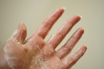 Fototapeta premium Wet female hand with foam on a beige background. Side view, closeup