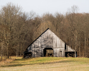 An old barn in an empty field surrounded by forest in the winter