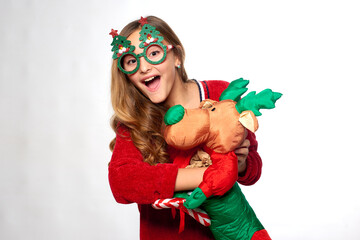 cheerful girl in Christmas costume and paper glasses holds toy sock in form of santa deer in hands and fools around