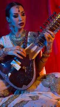 Beautiful young indian woman in traditional Sari clothing with Oriental Jewelry Playing the Sitar.
