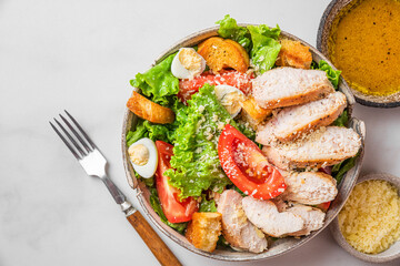 Chicken salad. Caesar salad with chicken breast fillet in a plate with fork and dressing on white background. Top view