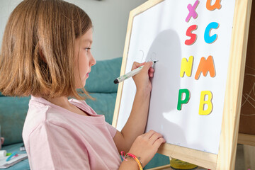 little girl drawing and learning the letters on a blackboard at home. Learn having fun.