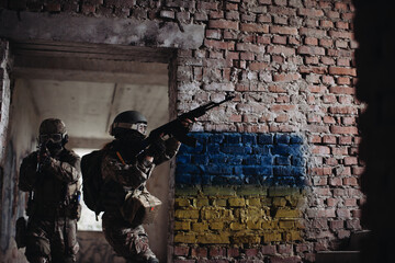 Ukrainian Soldiers military in the war with a weapon in his hands. The flag of Ukraine is painted on a brick wall. Relations between Ukraine and Russia