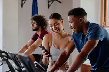 Fototapeta premium Three young multiracial friends laughing while on mobile phone at the gym