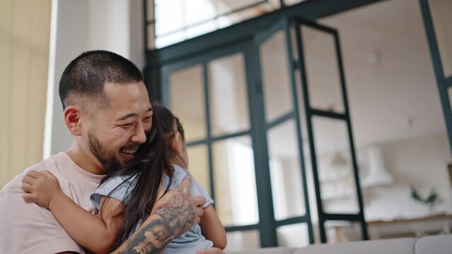 Asian daughter runs playing and hugging happy bearded father