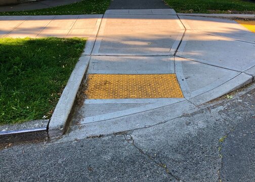A curb cut with a yellow textured section in the sidewalk provides accessibility for everyone