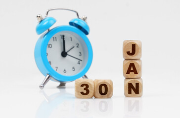 Wooden cube calendar for January 30, next to a blue alarm clock.