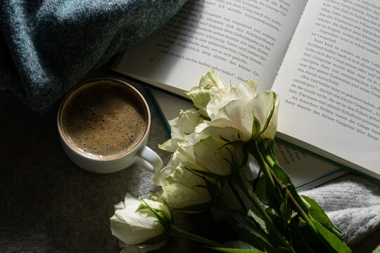 A cup of black hot coffee, an interesting book, a bouquet of white roses and a warm sweater for an autumn morning