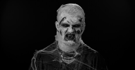 Sinister man with horrible scary Halloween zombie makeup in convulsions making faces, looking...