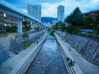 夕暮れの神戸市東灘区住吉川沿い。散歩をする人、水辺で涼む人。