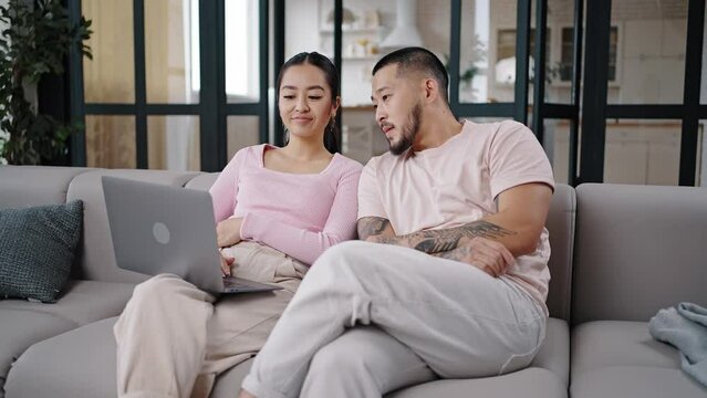 Asian couple sits searching information on laptop discussing