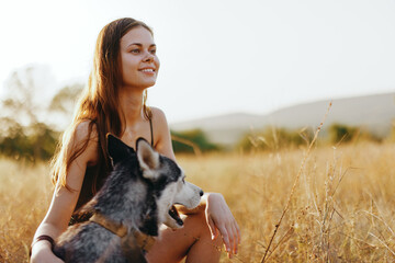 A woman strokes and hugs a husky dog ​​and smiles outside the house in nature in a field in...