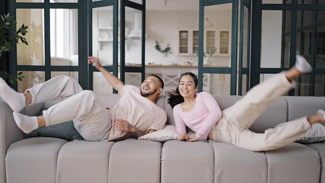 Asian couple jumps on grey couch enjoying successful life