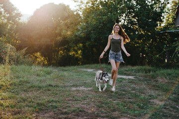 A woman runs with a dog in the forest during an evening walk in the forest at sunset in autumn. Lifestyle sports training with your beloved dog