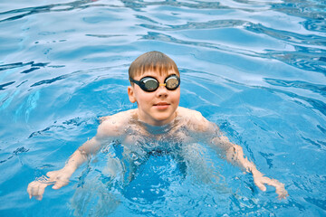 Fototapeta na wymiar Smiling boy portrait in swimming goggles, Child swim in the pool, sunbathes, swimming in hot summer day. Relax, Travel, Holidays, Freedom concept. 