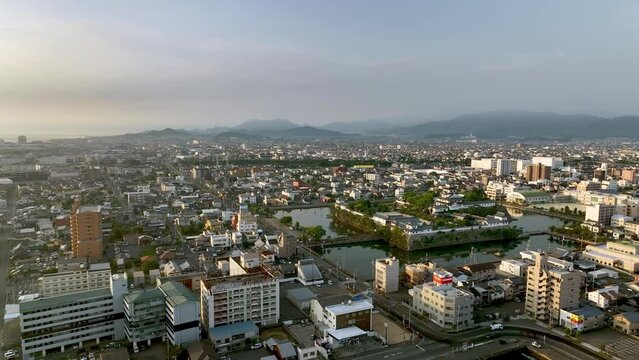 Slow move toward Japanese castle surrounded by moat and sprawling city in early morning light