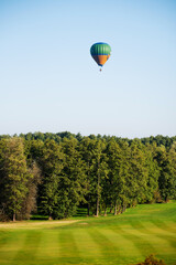 Colorful balloons fly over the green landscape of the field and trees