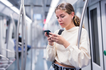 Focused girl riding on a subway train is texting with friends on her mobile phone