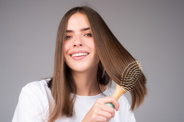 Portrait of beautiful young woman combing her hair, smiling. Female brushing healthy hair with comb.