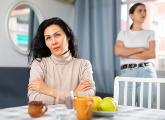 Upset disappointed woman sitting at home while girl calming her, asking to forgive after argument