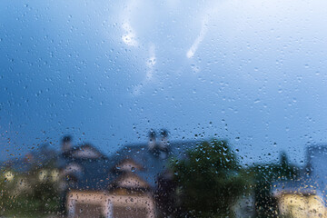 Rain drops on window glass and thunderstorm lightning blurred background