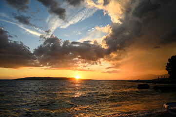 Golden sunset at the sea. Tropical sunset with dramatic sky with clouds. Sun going down in orange sky over horizon. Silhouette of a island. Soft waves on the water.
