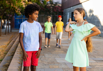 Young african-american boy and caucasian girl walking during summer day and having conversation.