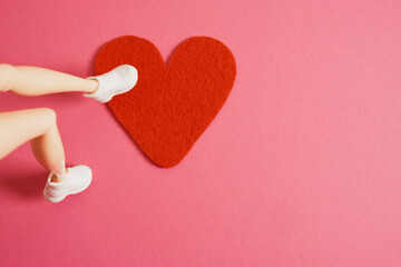 female doll's legs ad red felt heart on pink background