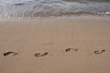 Footprints at golden sand, footsteps. Sea background, nature of tropical summer beach with rays of sun light. Sand beach, sea water with copy space, summer vacation concept.
