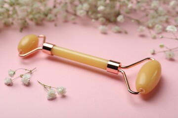 Natural face roller and flowers on pink background