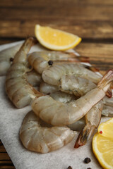 Fresh raw shrimps with lemon on wooden board, closeup