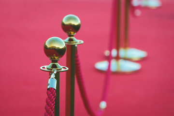 Red carpet with ropes and golden barriers on a luxury party entrance, cinema premiere film festival event gala ceremony, wealthy rich guests arriving, outdoor decoration elements, summer sunny day