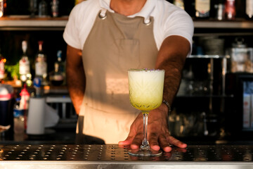 Bartender serving fresh yellow, white summer fruit cocktail at bar counter on sunny day. 