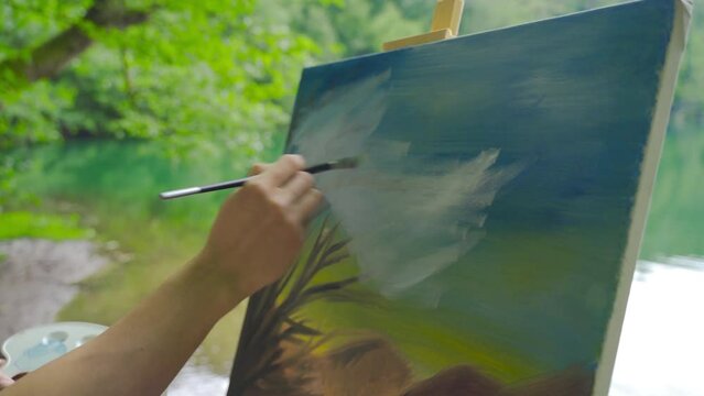 Close-up painter painting a picture by the lake.
Painter painting against a lake landscape.
