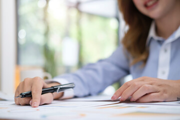 Close up view businesswoman hand holding pen and checking financial reports on office desk.