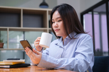 Pleasant asian woman employee sitting in corporate office and using smart phone.