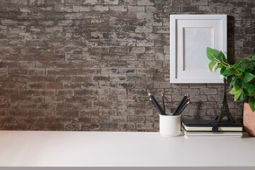 Stylish workplace with picture frame, coffee cup houseplant and stationery on white table. Copy space for your advertise text.