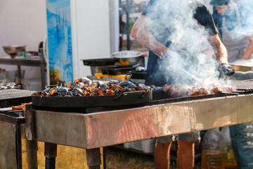 Defocus man cooking bbq meat at festival outdoor. Seafood paella. Chef grilling sausages in park outside. Concept of summer party with families and friends. Out of focus