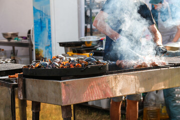 Defocus man cooking bbq meat at festival outdoor. Seafood paella. Chef grilling sausages in park...