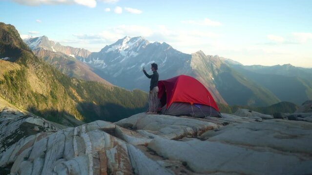 Young caucasian male filming epic sunrise mountain views with phone outside of tent