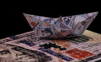 Paper boat with the image of banknotes in denominations of 100 American dollars on a black background